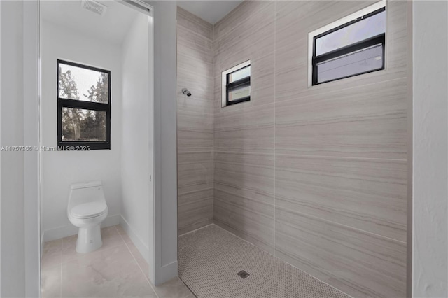 full bathroom with plenty of natural light, a tile shower, toilet, and tile patterned floors