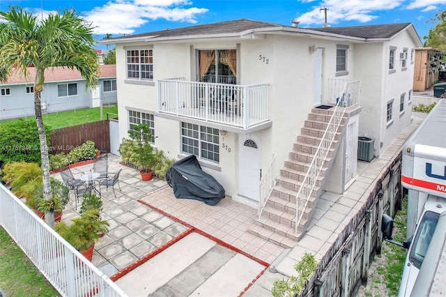 rear view of house with a fenced backyard, a balcony, central AC, stucco siding, and a patio area