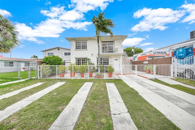 back of property with a fenced front yard, a lawn, a balcony, and stucco siding