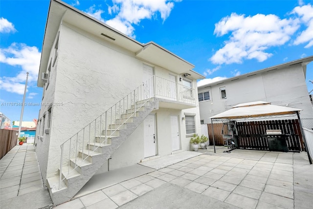 back of house featuring a patio, stucco siding, stairway, a gazebo, and fence