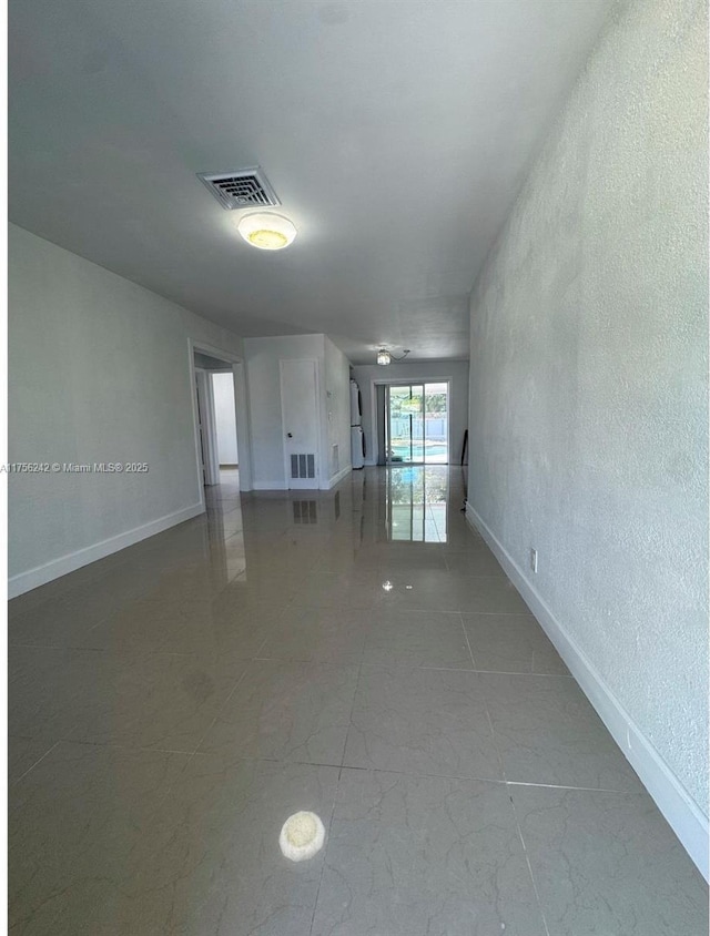 unfurnished living room featuring a textured wall, visible vents, and baseboards