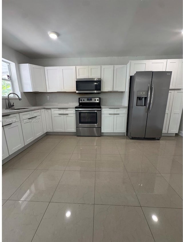 2318 Scott St, Hollywood, FL 33020 - kitchen with appliances with stainless steel finishes, white cabinetry, light marble finish flooring, and light countertops
