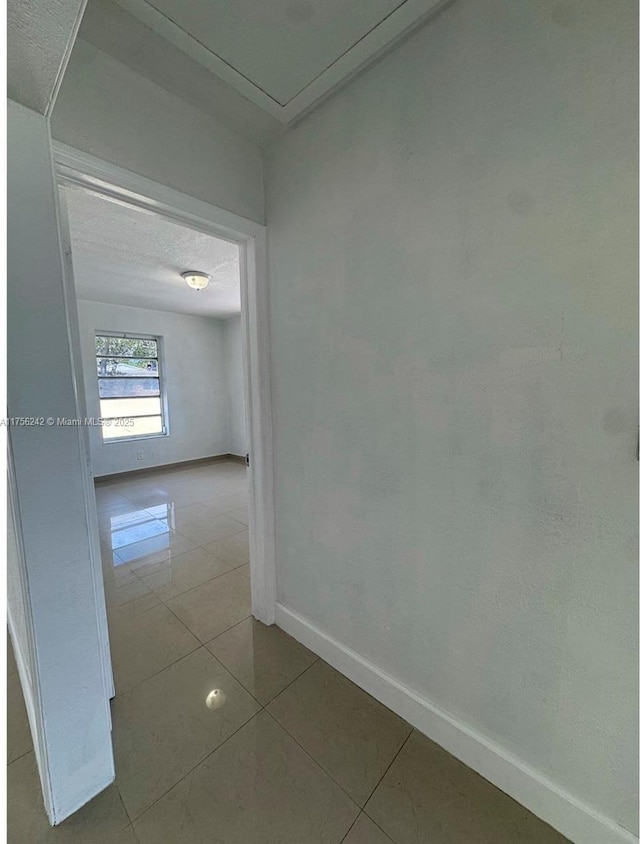 hall featuring a textured ceiling, tile patterned floors, and baseboards