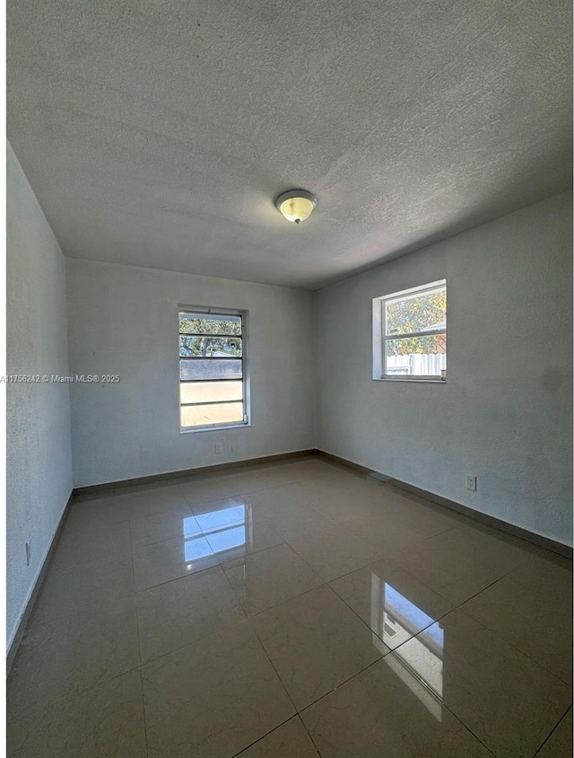 tiled empty room with plenty of natural light, baseboards, and a textured ceiling