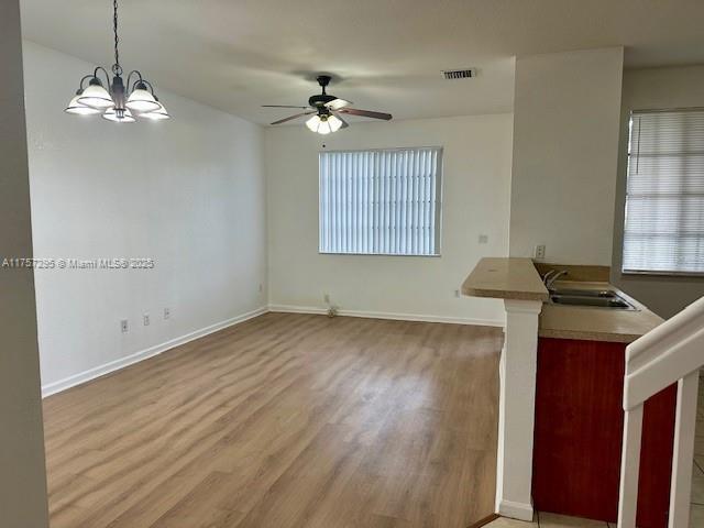 unfurnished living room featuring visible vents, a sink, baseboards, and wood finished floors