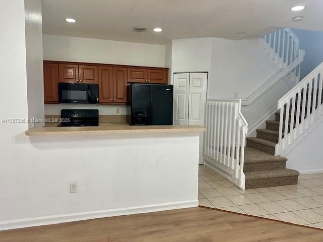 kitchen featuring a peninsula, visible vents, light countertops, light wood-type flooring, and black appliances