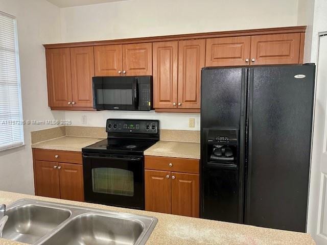 kitchen with brown cabinets, black appliances, light countertops, and a sink