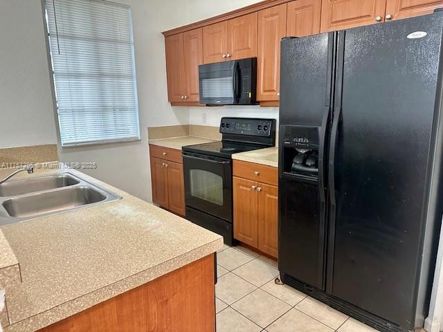 kitchen featuring light tile patterned floors, a sink, light countertops, brown cabinets, and black appliances