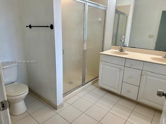 bathroom with double vanity, toilet, tile patterned floors, a shower stall, and a sink