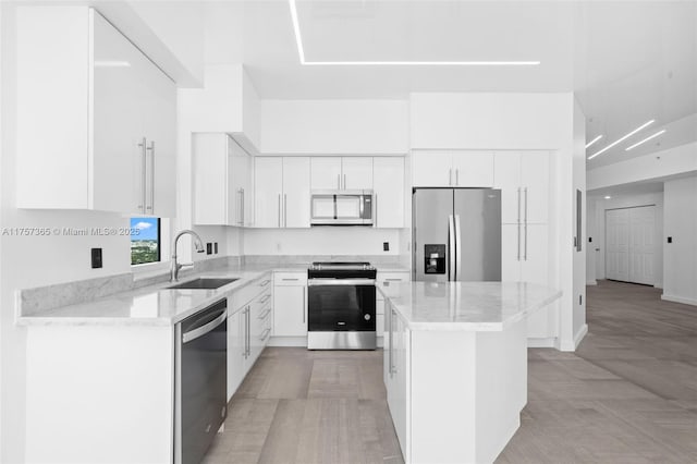 kitchen with stainless steel appliances, a sink, white cabinetry, a center island, and light stone countertops