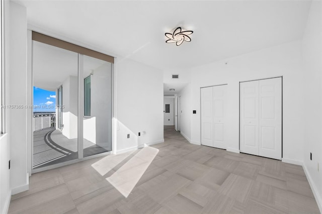 unfurnished bedroom with baseboards, visible vents, access to exterior, a wall of windows, and two closets