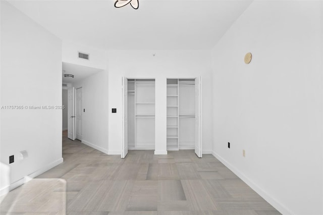 unfurnished bedroom featuring two closets, visible vents, and baseboards