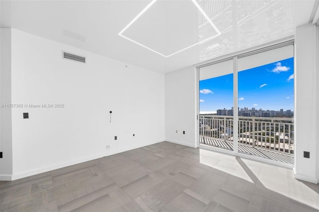 empty room with expansive windows, visible vents, a city view, and baseboards