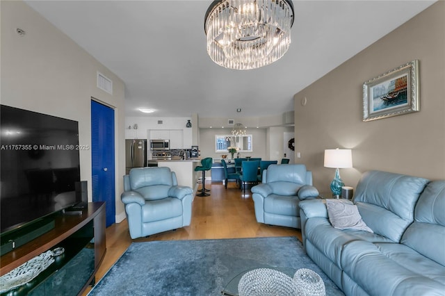 living room with light wood finished floors, visible vents, and a notable chandelier