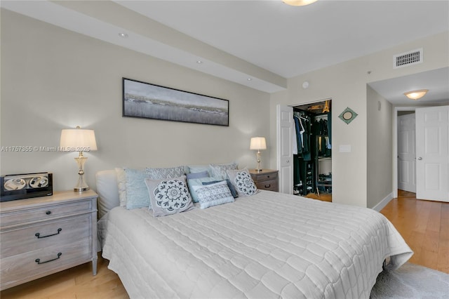 bedroom with a closet, visible vents, a spacious closet, wood finished floors, and baseboards