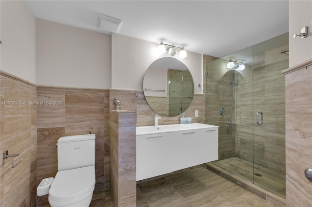 bathroom featuring tile walls, visible vents, toilet, a shower stall, and vanity