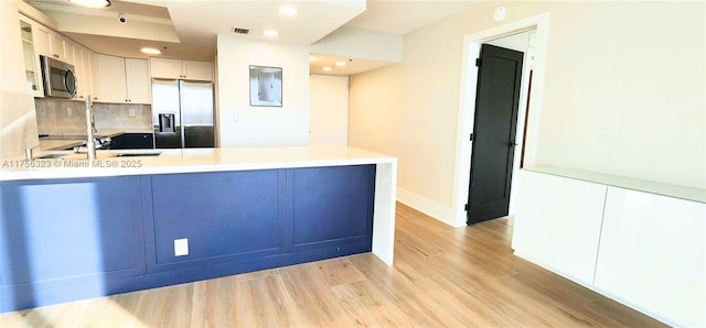 kitchen featuring decorative backsplash, light wood-style flooring, appliances with stainless steel finishes, a peninsula, and light countertops