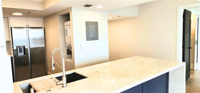 kitchen featuring stacked washer and dryer, visible vents, electric panel, light wood finished floors, and stainless steel fridge