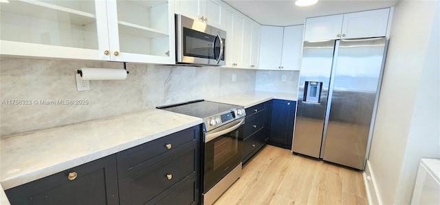 kitchen featuring light wood-style flooring, stainless steel appliances, white cabinets, decorative backsplash, and glass insert cabinets