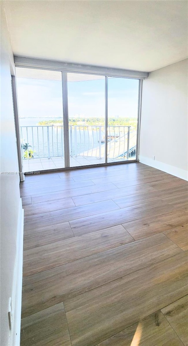 empty room featuring expansive windows, baseboards, and wood finished floors