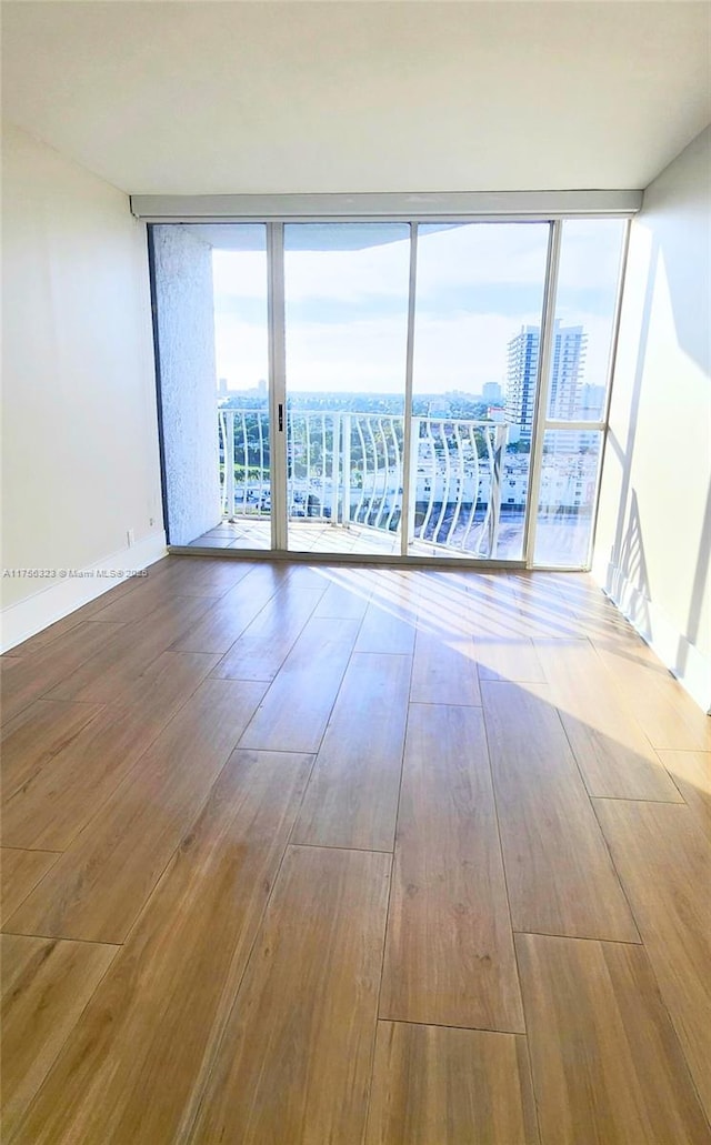 empty room with a wall of windows, a view of city, a healthy amount of sunlight, and wood finished floors