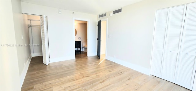 unfurnished bedroom featuring a walk in closet, a closet, visible vents, and light wood-style flooring