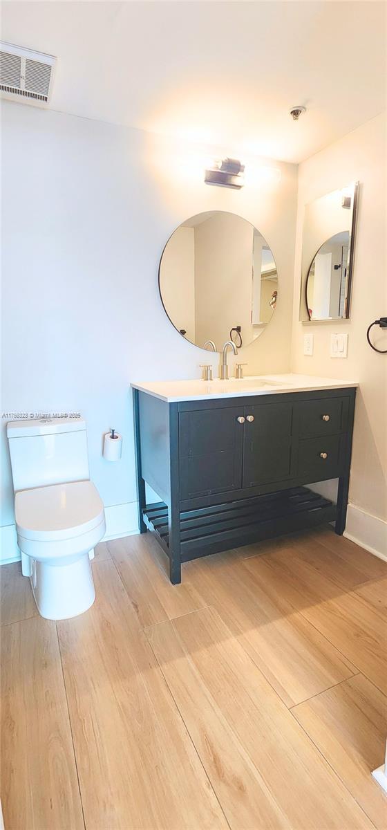 bathroom featuring baseboards, visible vents, toilet, wood finished floors, and vanity