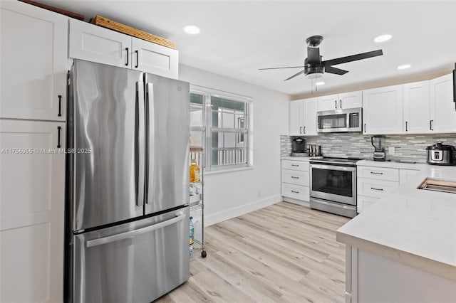 kitchen with tasteful backsplash, white cabinets, light wood-style flooring, appliances with stainless steel finishes, and light countertops