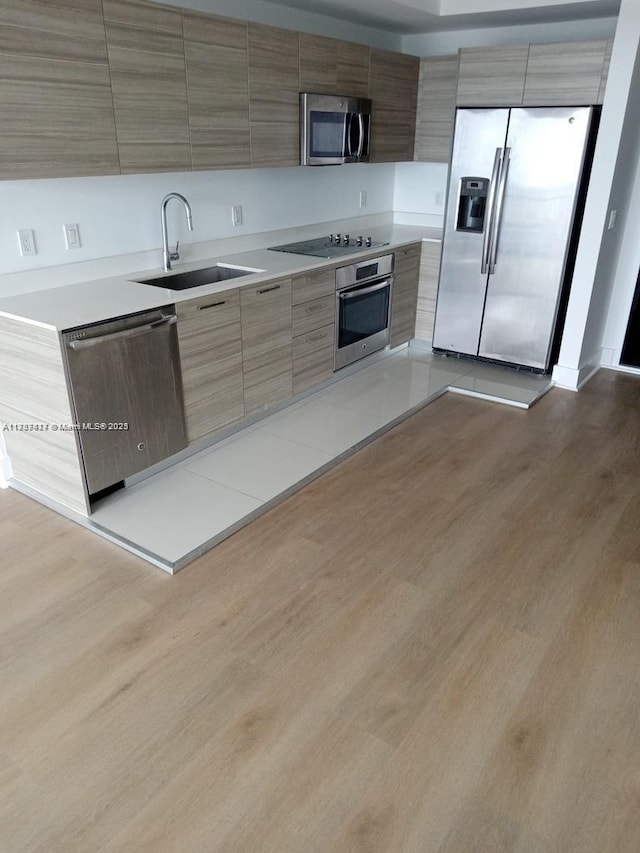 kitchen with light wood-type flooring, modern cabinets, appliances with stainless steel finishes, and a sink