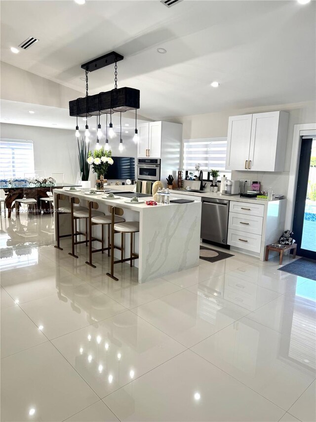 kitchen featuring visible vents, white cabinets, a spacious island, a breakfast bar area, and stainless steel appliances