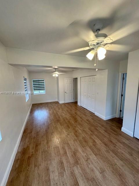 unfurnished bedroom with multiple closets, ceiling fan, baseboards, and wood finished floors