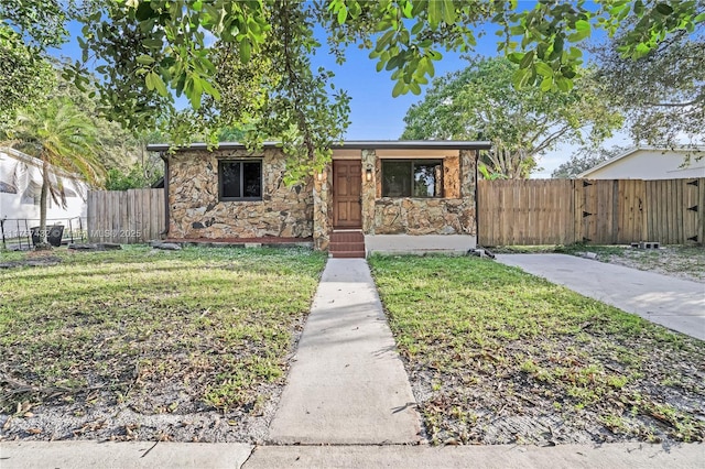 view of front of home featuring stone siding, fence, and a front lawn