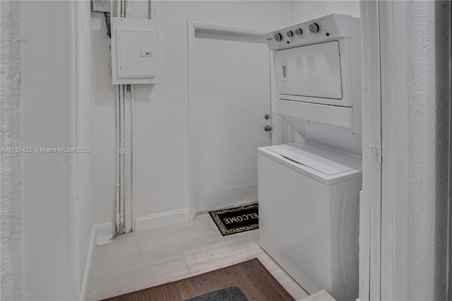 laundry area featuring stacked washer / dryer, wood finished floors, laundry area, electric panel, and baseboards