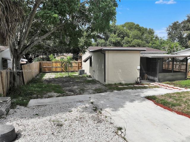 exterior space featuring cooling unit, stucco siding, a sunroom, fence private yard, and driveway