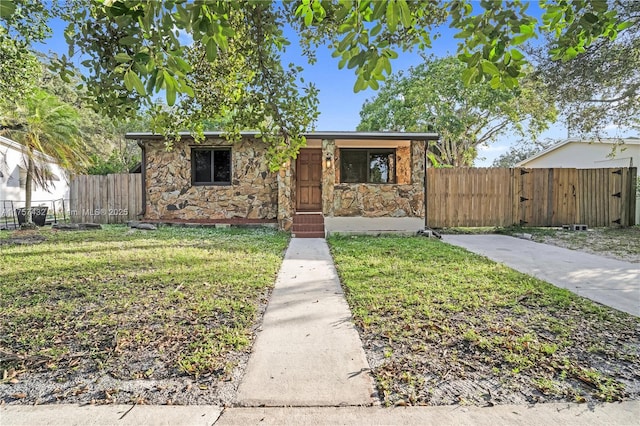 view of front of property featuring a front yard, stone siding, and fence