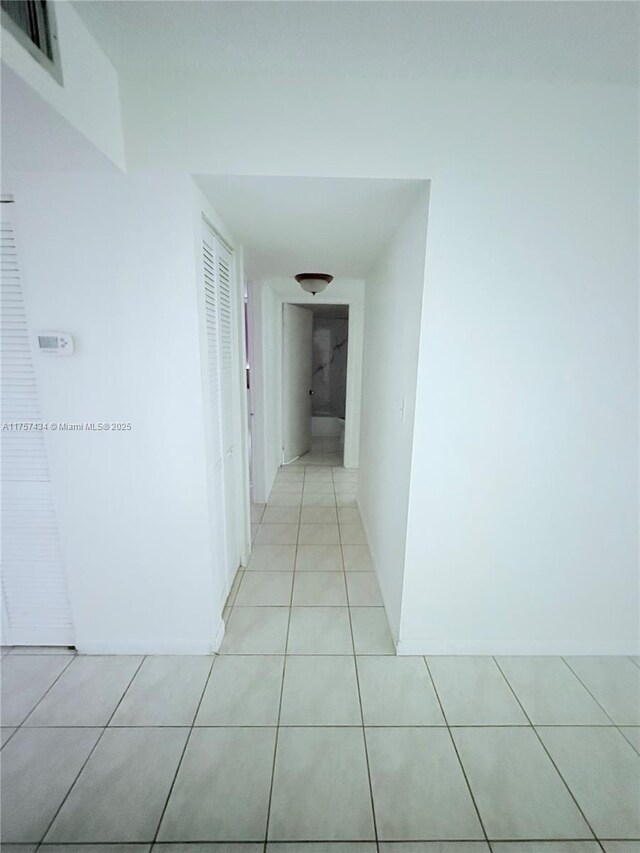 hall featuring baseboards, visible vents, and light tile patterned floors