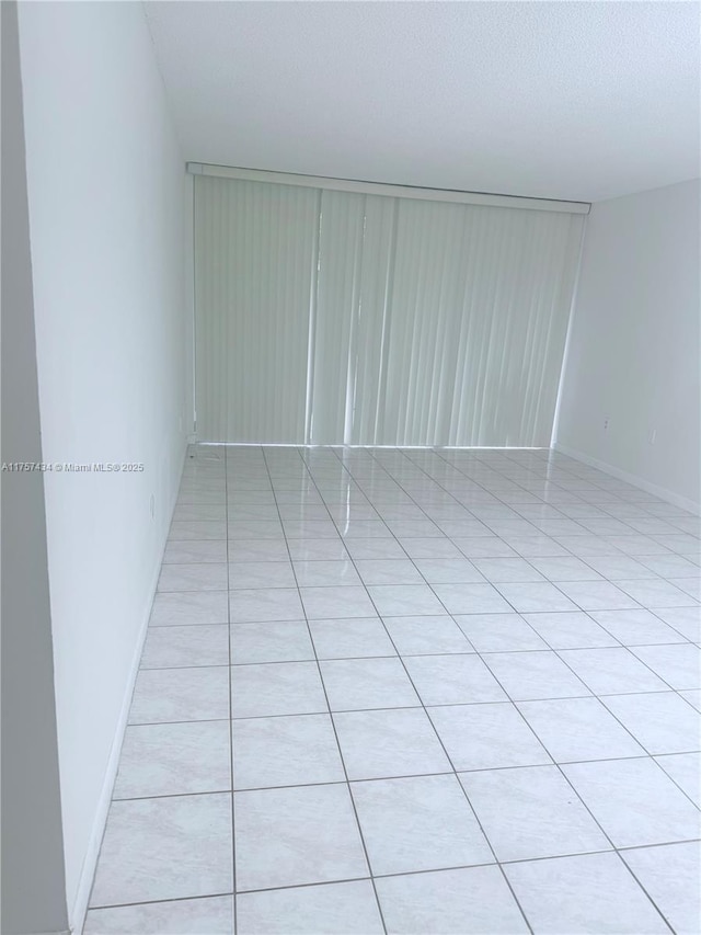 unfurnished room with baseboards, a textured ceiling, and light tile patterned flooring