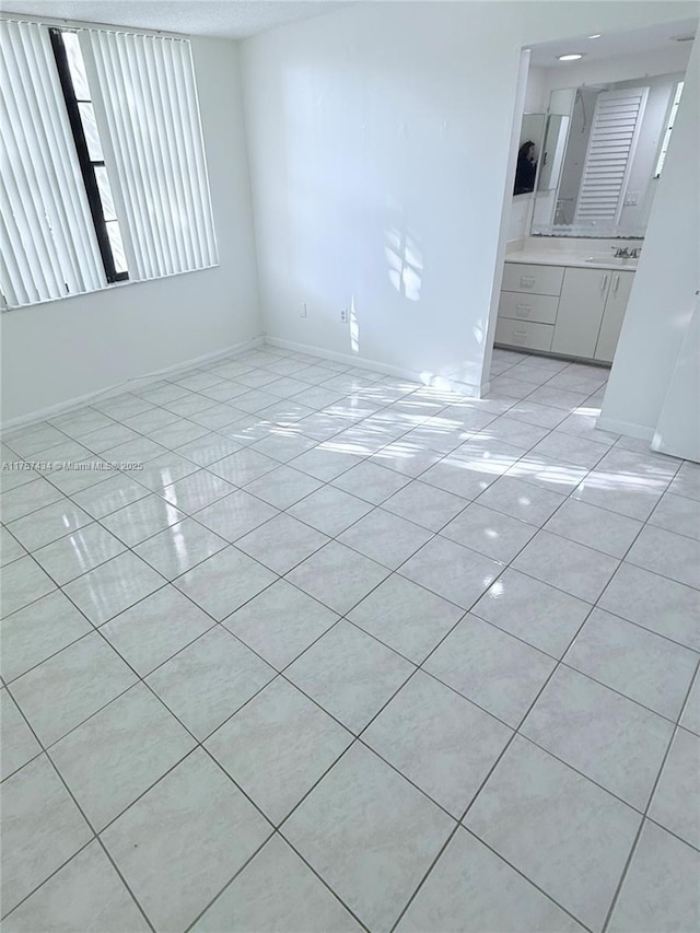 unfurnished living room with light tile patterned floors, baseboards, and a sink