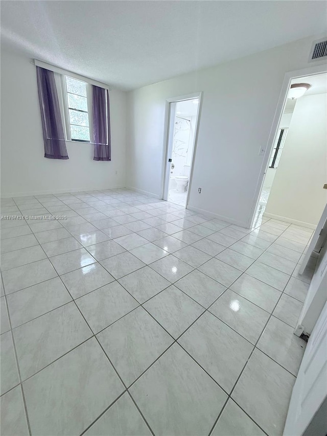 empty room with baseboards, visible vents, a textured ceiling, and light tile patterned floors