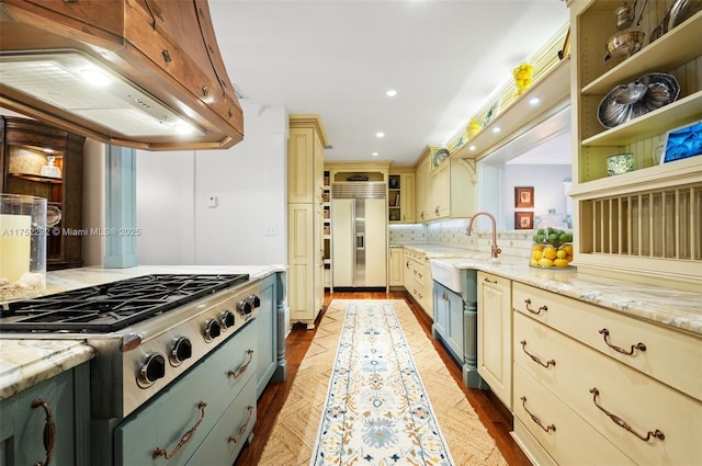 kitchen with cream cabinetry, stainless steel gas stovetop, a sink, built in refrigerator, and extractor fan