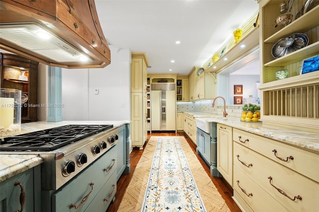 kitchen featuring stainless steel gas cooktop, built in fridge, range hood, cream cabinetry, and a sink