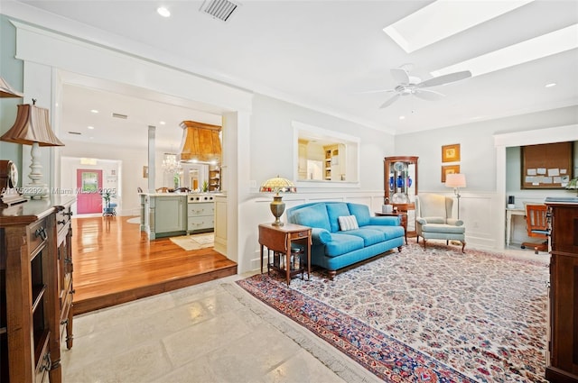 living area with visible vents, a wainscoted wall, a skylight, a decorative wall, and ceiling fan