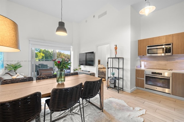 kitchen featuring light countertops, light wood-style flooring, appliances with stainless steel finishes, brown cabinetry, and high vaulted ceiling