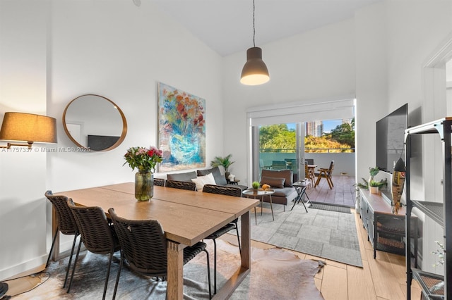 dining room featuring light wood-style floors, a towering ceiling, and baseboards