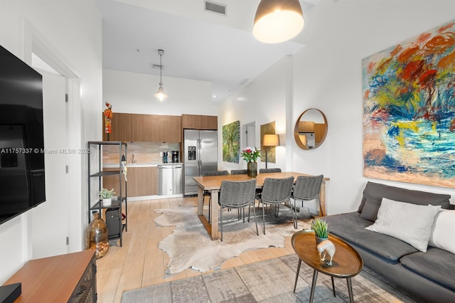 living area featuring visible vents, a towering ceiling, and light wood finished floors