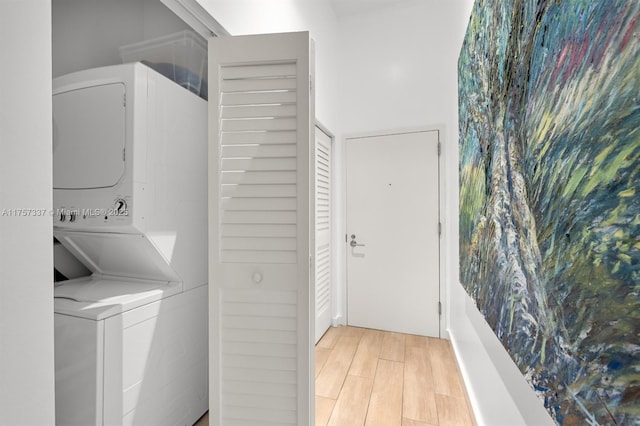 clothes washing area with laundry area, light wood finished floors, and stacked washer and clothes dryer