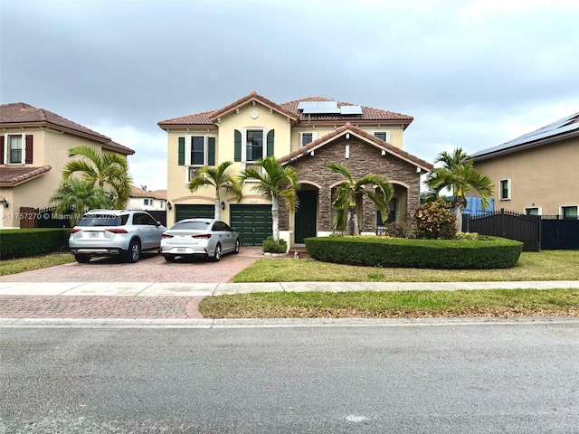 view of front of house featuring decorative driveway, stucco siding, an attached garage, roof mounted solar panels, and fence