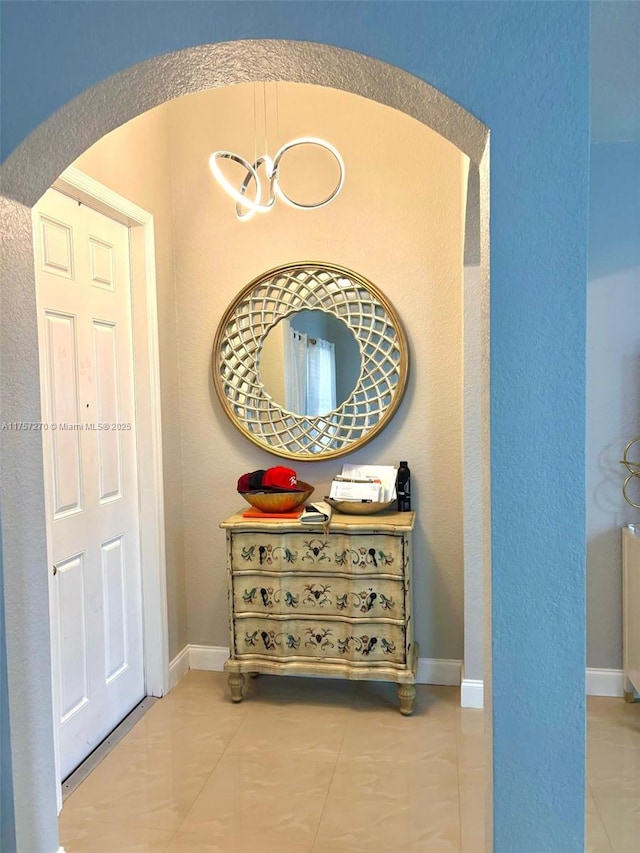 corridor with baseboards, arched walkways, and tile patterned floors