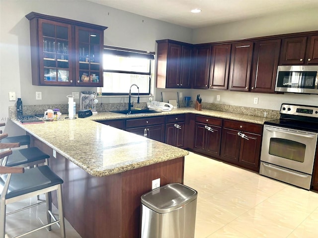 kitchen with a breakfast bar area, appliances with stainless steel finishes, glass insert cabinets, a sink, and a peninsula