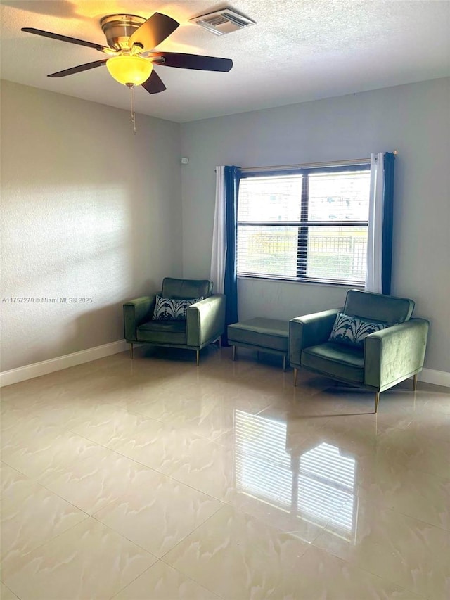 living area featuring a ceiling fan, visible vents, a textured ceiling, and baseboards